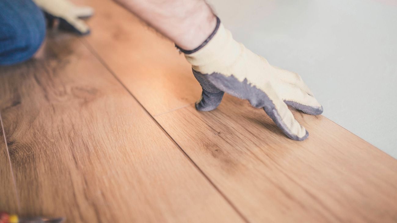 A gloved hand aligning a floating wooden floorboard.