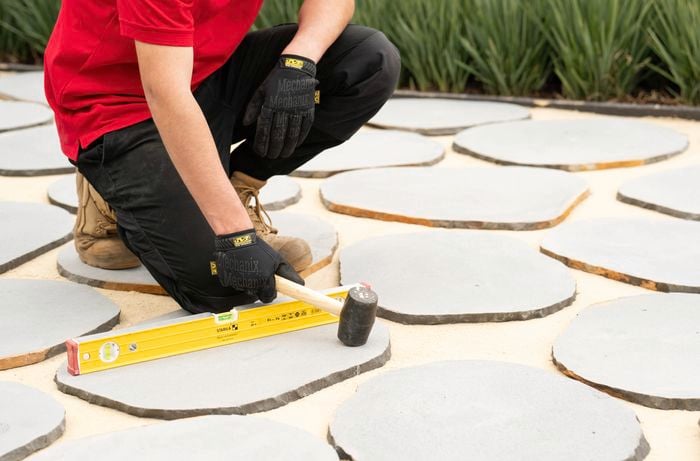 A person is laying the tuscan path stepping stones onto the sand bed using a rubber mallet.