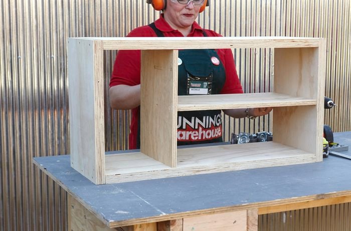 A person fitting a shelf into an open timber shelving unit