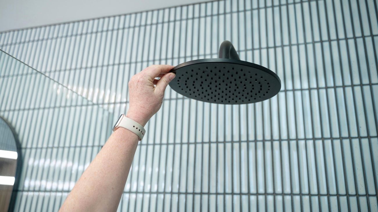 A person touching a black shower head.
