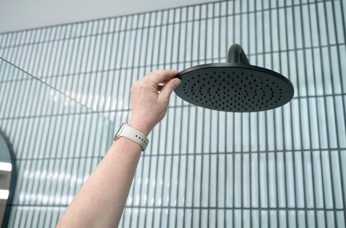 A person touching a black shower head.