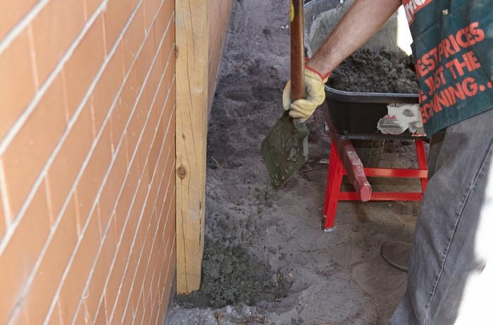 A person filling a post hole with concrete next to a brick wall