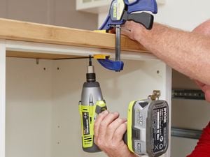 Person attach a benchtop to cabinets using a cordless drill and clamp