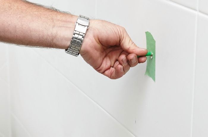 A person inserting a wall plug into a holes in a tiled wall