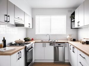Modern light kitchen with venetian blinds and timber benchtops.