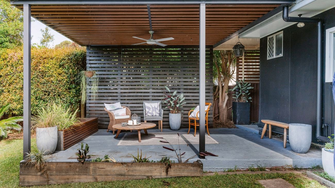 Covered outdoor patio with seating area, potted plants, and timber slat privacy screen