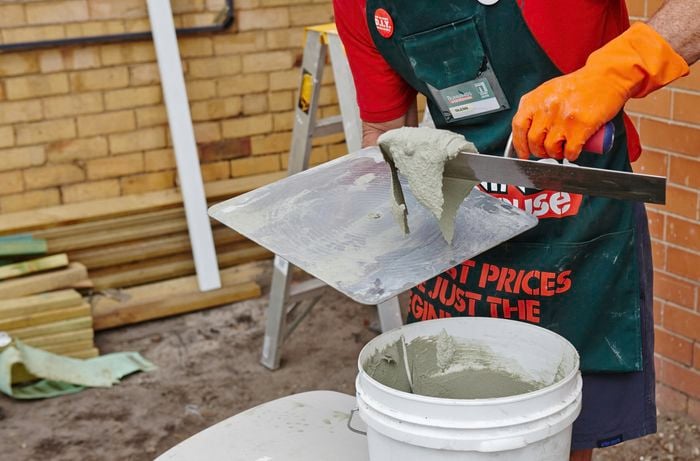 A person putting render mix onto a hawk with a trowel