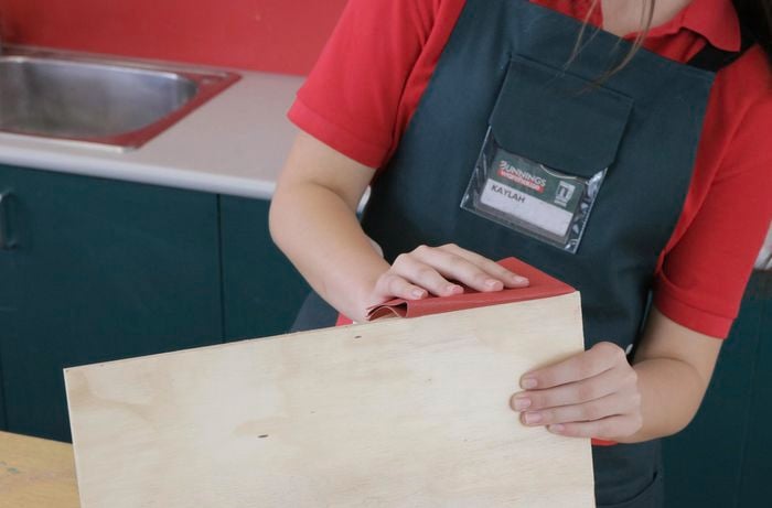 Woman sanding the edge of a sheet of plywood