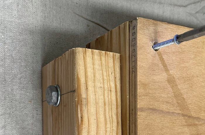A screw being driven into a piece of plywood with a drill, next to a wooden block.