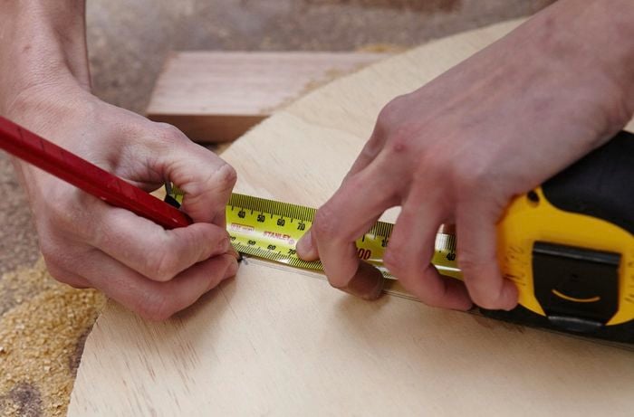 A person marking a measurement on a round sheet of plywood