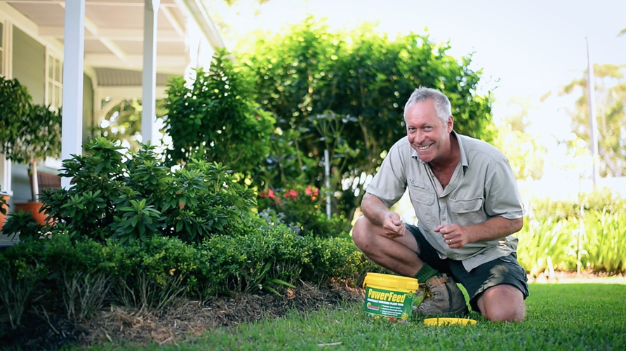Smiling man kneeling in garden applying plant food