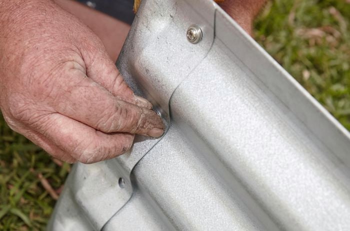 Person screwing corrugated iron garden bed sides together.