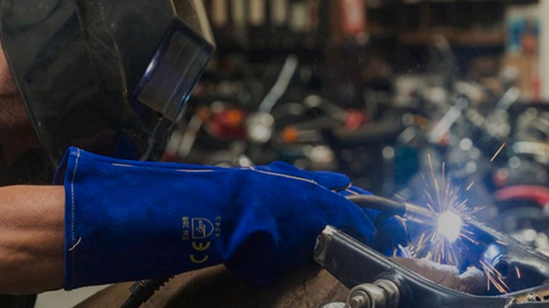 Person welds gas wearing protective clothing and gear.