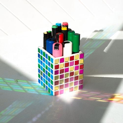 Pen holder mosaiced with coloured metallic glass. The light is reflecting colours onto the surface below. 