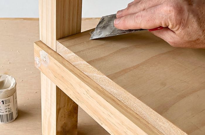  A person uses timber filler to fill the screw heads in a timber frame.