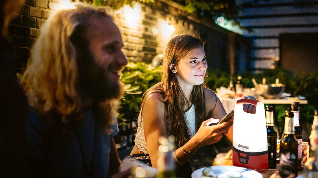 A man and a woman seated at a table in an outdoor dining setting, illuminated by an Energizer outdoor lantern