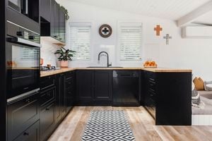 All-black kitchen design with timber benchtop and floorboards with black appliances and cabinetry
