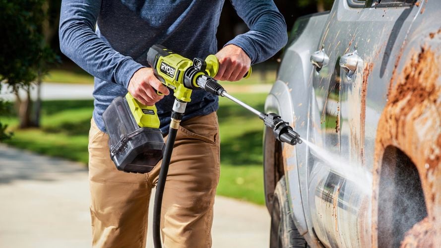 A person using a power pressure washer to clean a vehicle.