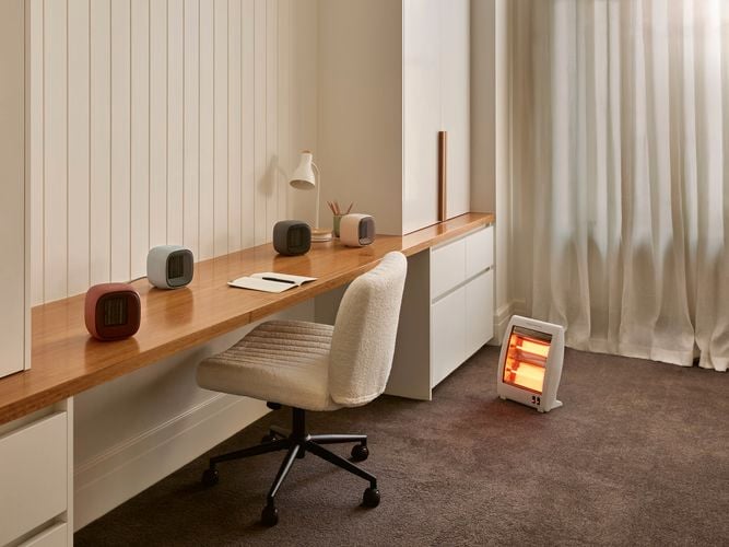 A room with a chair at a bench, a heater in it and carpet on the floor.