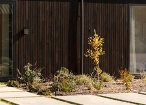 A modern house with a dark corrugated roof and landscaped garden.   