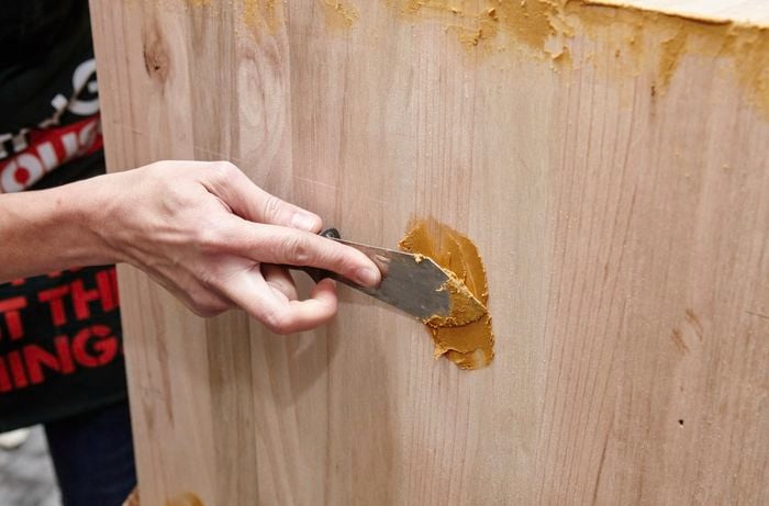 A person filling holes in a timber panel using wood putty
