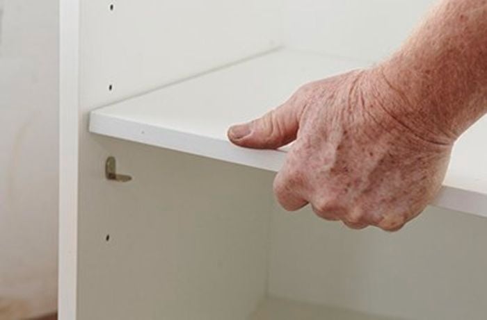 A shelf being laid in a cabinet