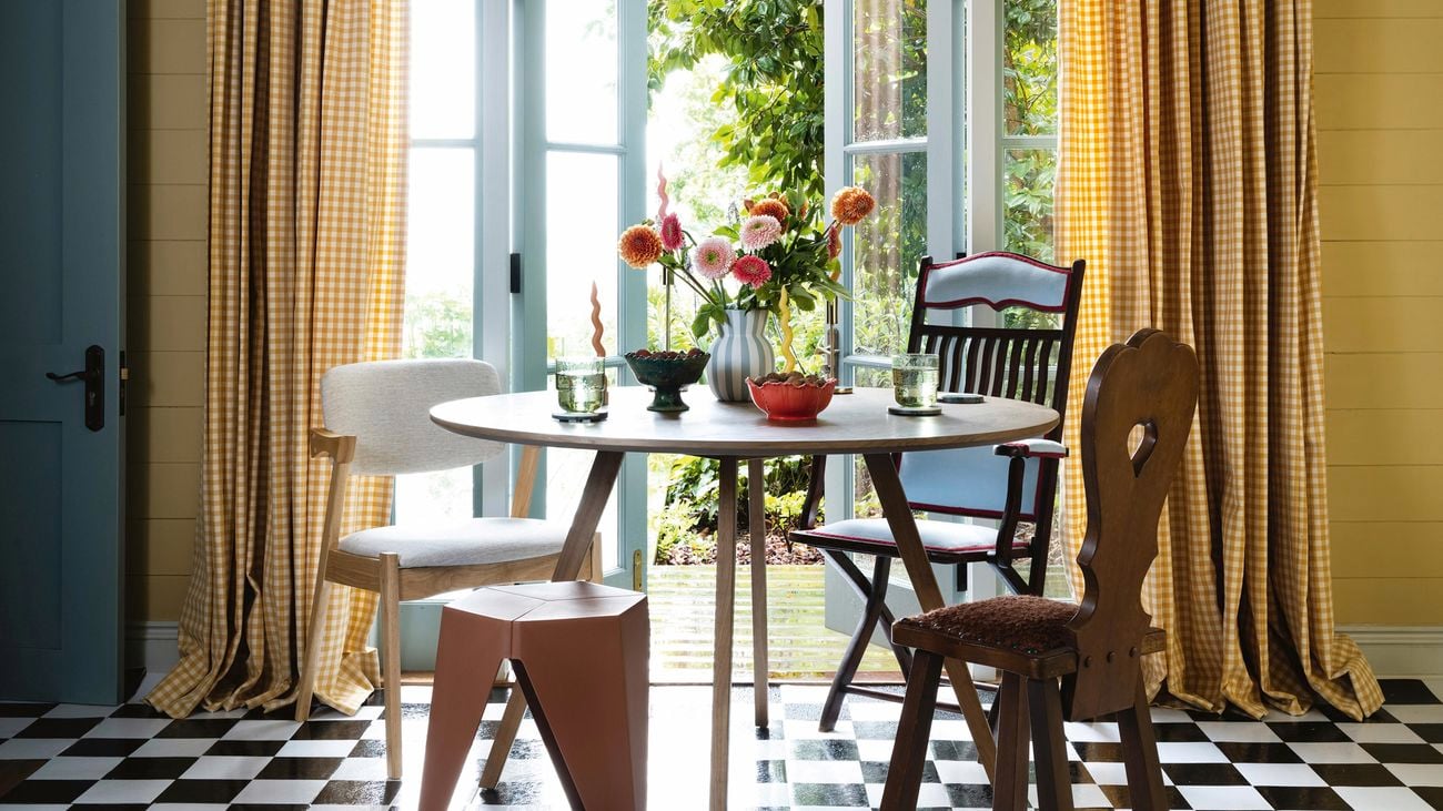 Dining room with checkerboard tiling, yellow curtains, red and white stripe hanging light and wooden dining set in the middle of the room.