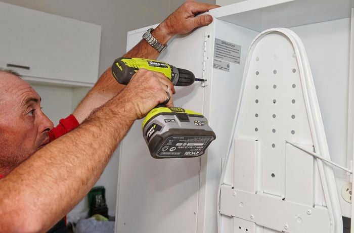 A Bunnings team member using the drill and screws to attach the door to the ironing centre.