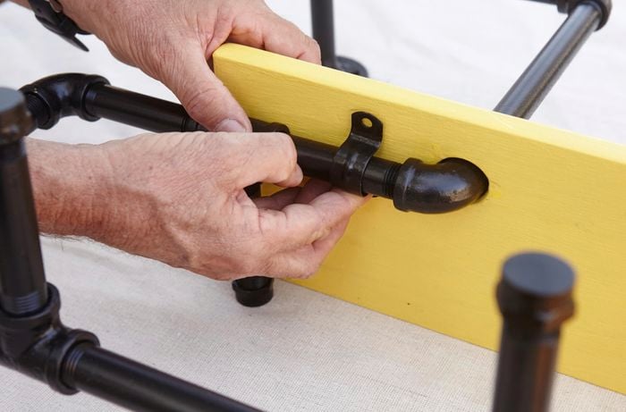 A yellow painted shelf being fixed to an ironing board storage rack