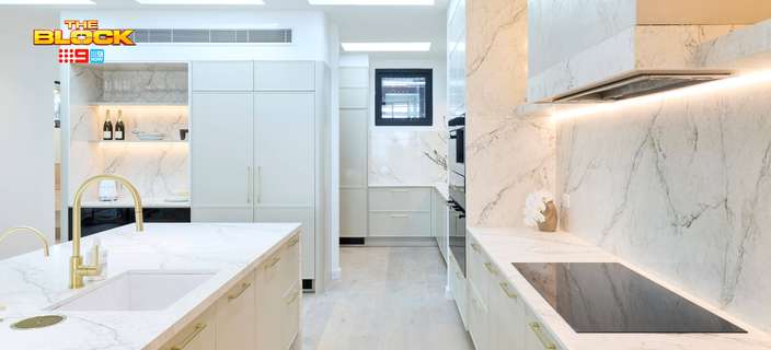 Modern kitchen featuring marble-look benchtops and splashbacks, neutral cabinetry, gold tapware and an integrated cooktop.