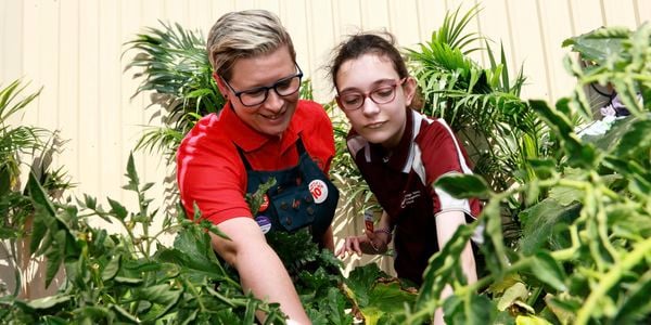 A Bunnings Team Member and a girl amongst plants in front of a fence outside.