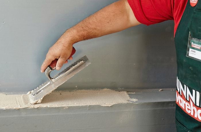 Tile adhesive being applied to a shelf with a notched trowel by a Bunnings team member