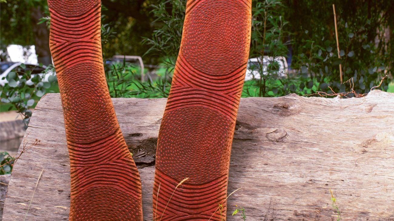 Two wood carvings sitting on grass in front of a large log.