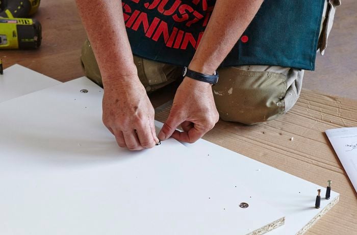 A person inserting a cam lock into the base panel of a cabinet
