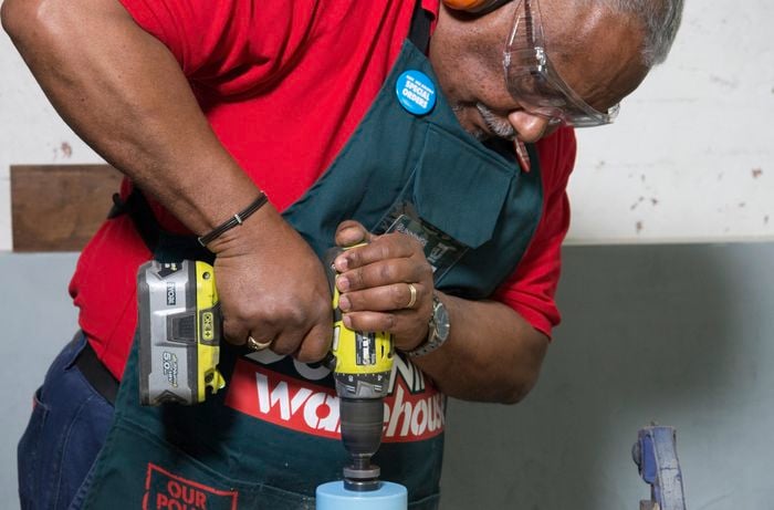 A person cutting a large circle from plywood using a hole saw