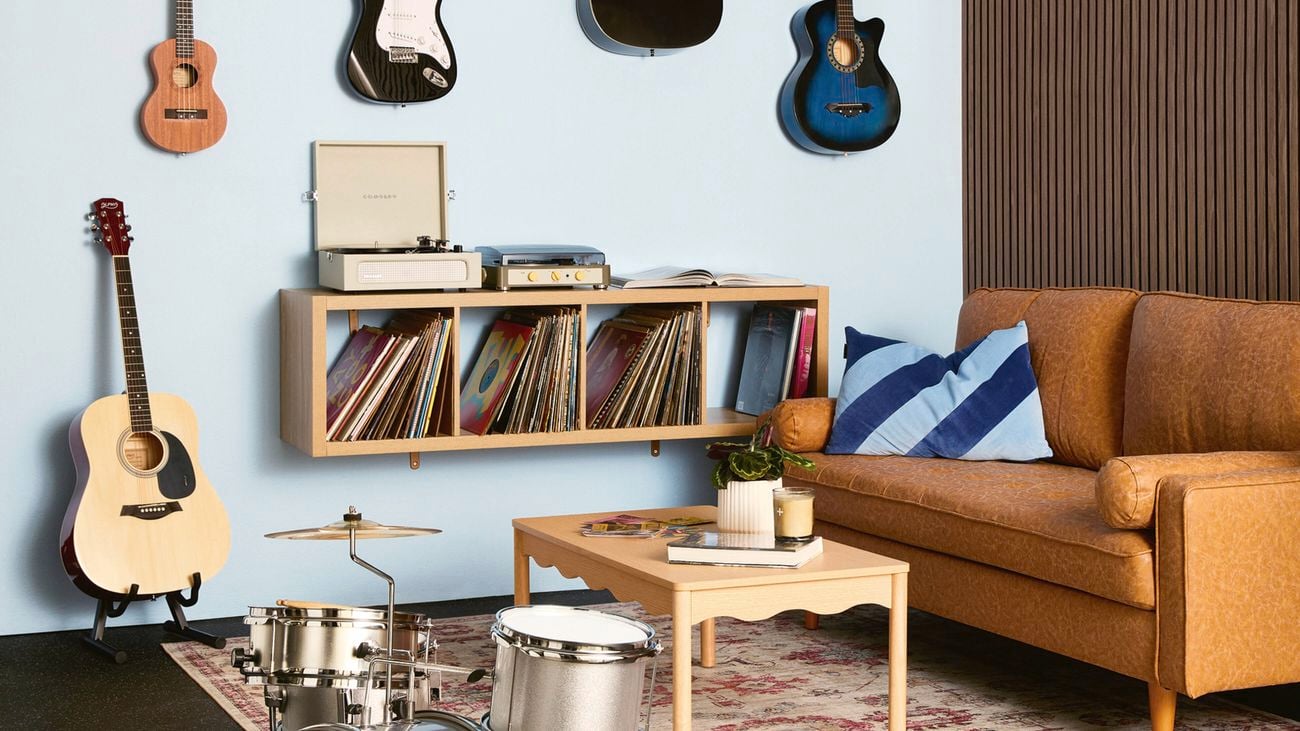 A music room with acoustic wall panelling, rubber floor matting, a tan sofa, drum kit, record player on floating shelves and wall-mounted guitars