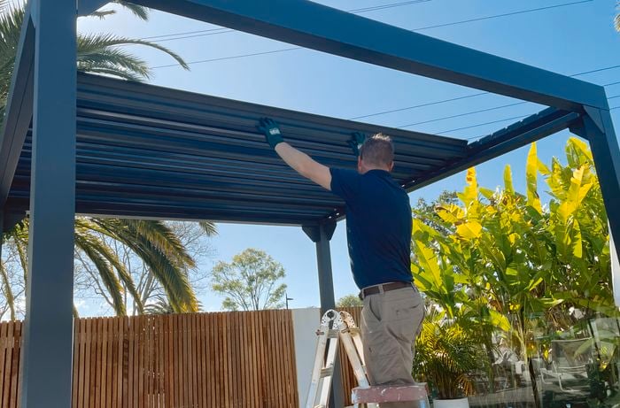 Person on a step ladder placing lourves on a gazebo.