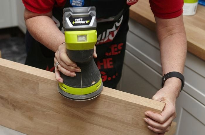 A person sanding the edge of a timber shelf