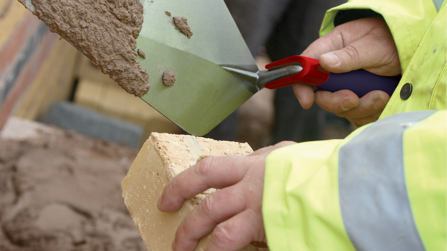 Close up of person putting mortar on a brick using a trowel