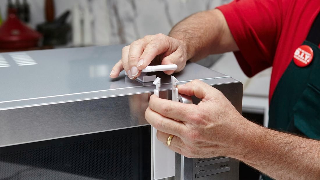 A person attaching a childproof lock to a microwave oven
