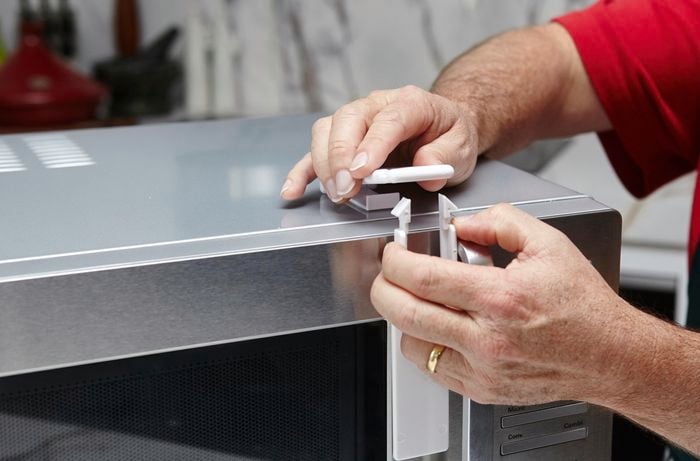 A person attaching a childproof lock to a microwave oven