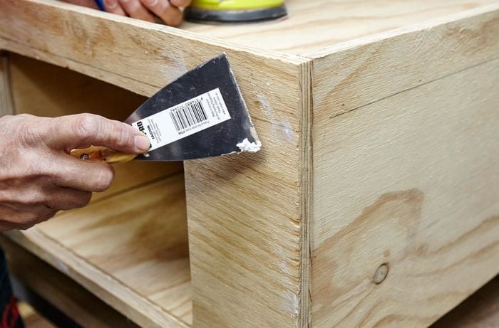 Person adding putty to fill holes in timber