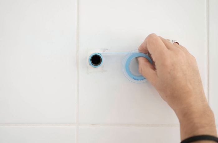 A hand is wrapping thread seal around the shower arm thread.