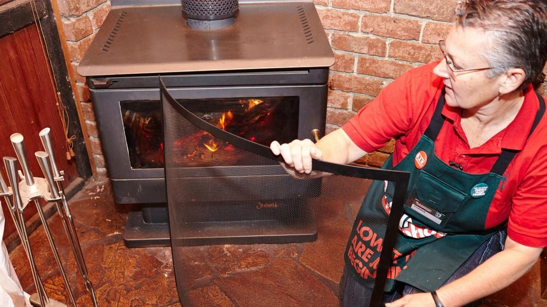 A person positioning a safety screen in front of a wood heater