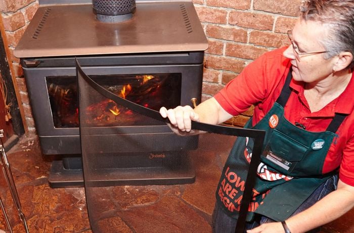 A person positioning a safety screen in front of a wood heater
