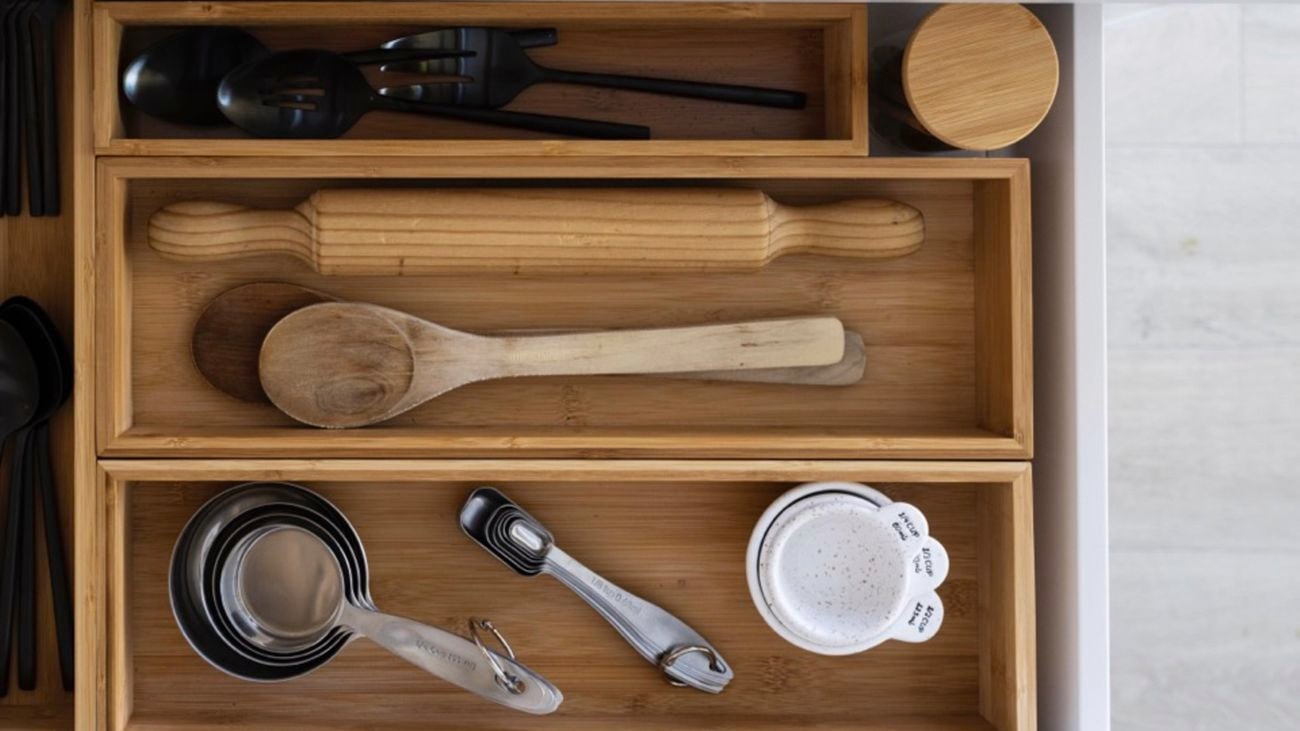A kitchen bench with a cutting board, recipe book and herbs on it. A drawer is pulled out showing utensils in wooden boxes.