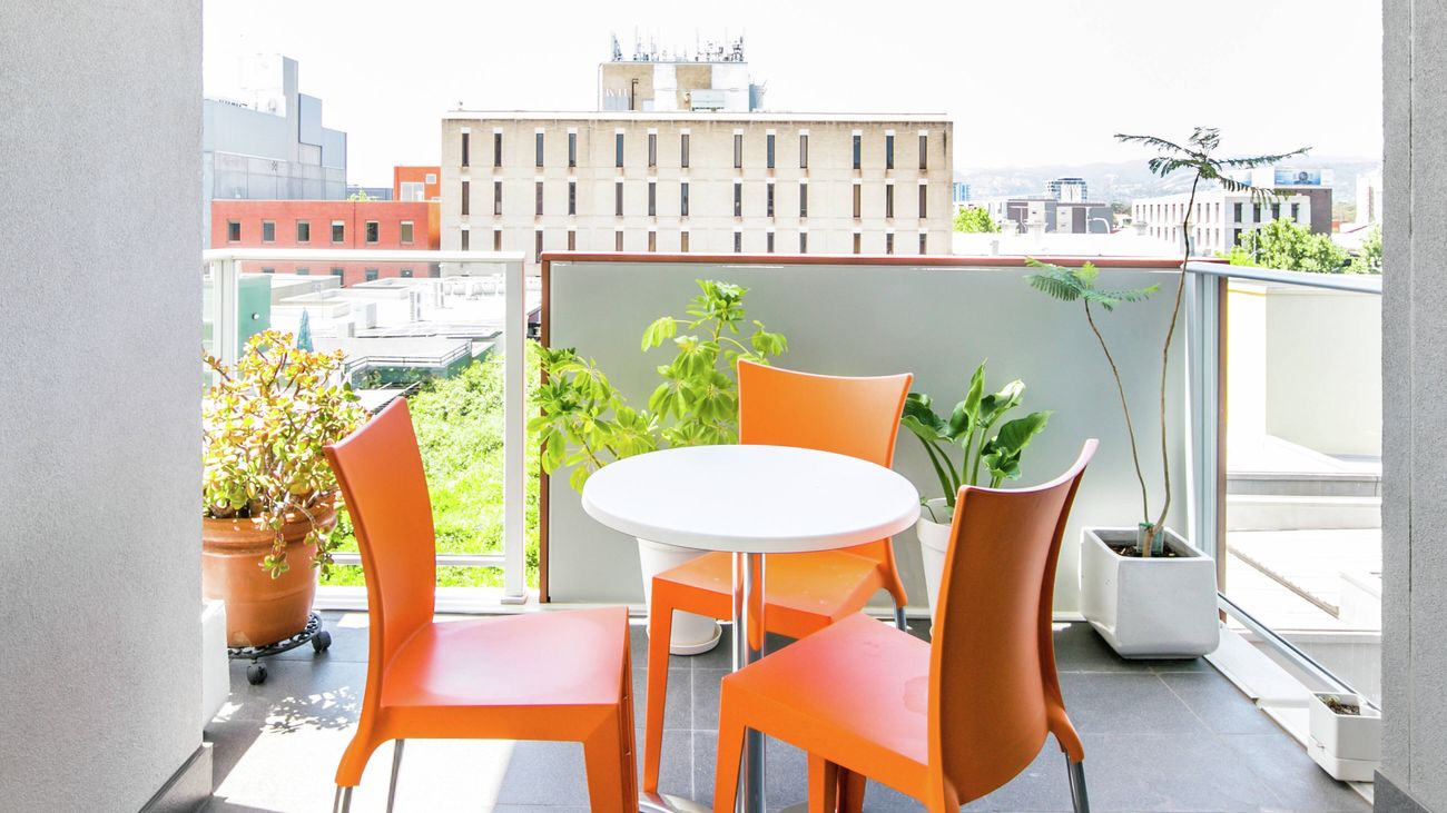 Balcony with a small table, orange chairs, potted plants and a city view.