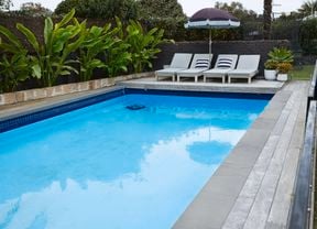 A swimming pool with pool chairs and umbrella.