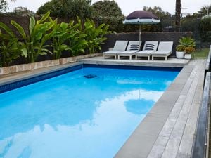 A swimming pool with pool chairs and umbrella.