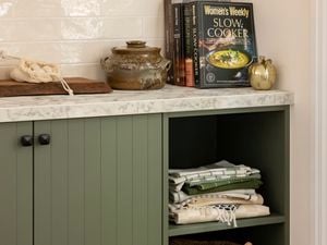 Kitchen with a marble benchtop with green cupboards underneath it, with blankets and a basket in them.